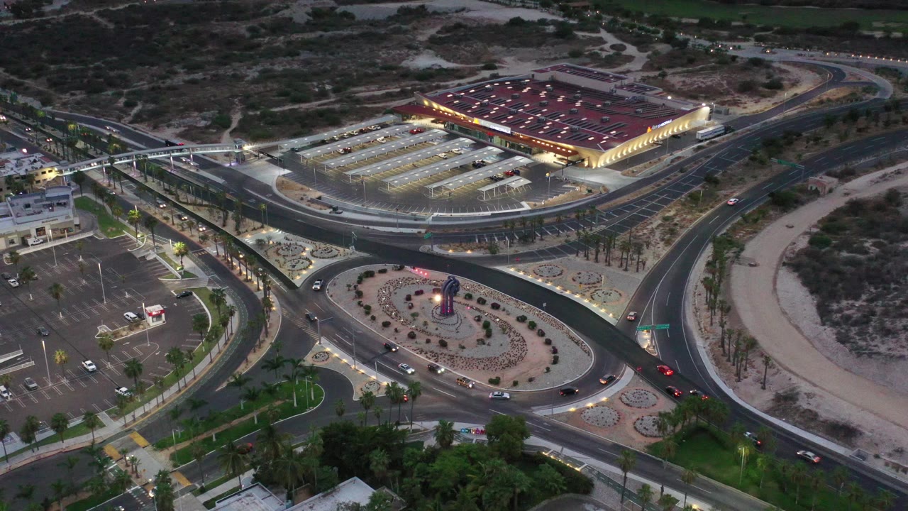 Drone view of dusk traffic lanes around a landscaped roundabout near a large building.