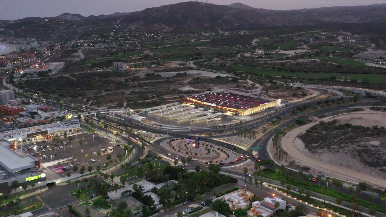 Aerial dusk view of roads, lit commercial buildings, dry land, and mountains