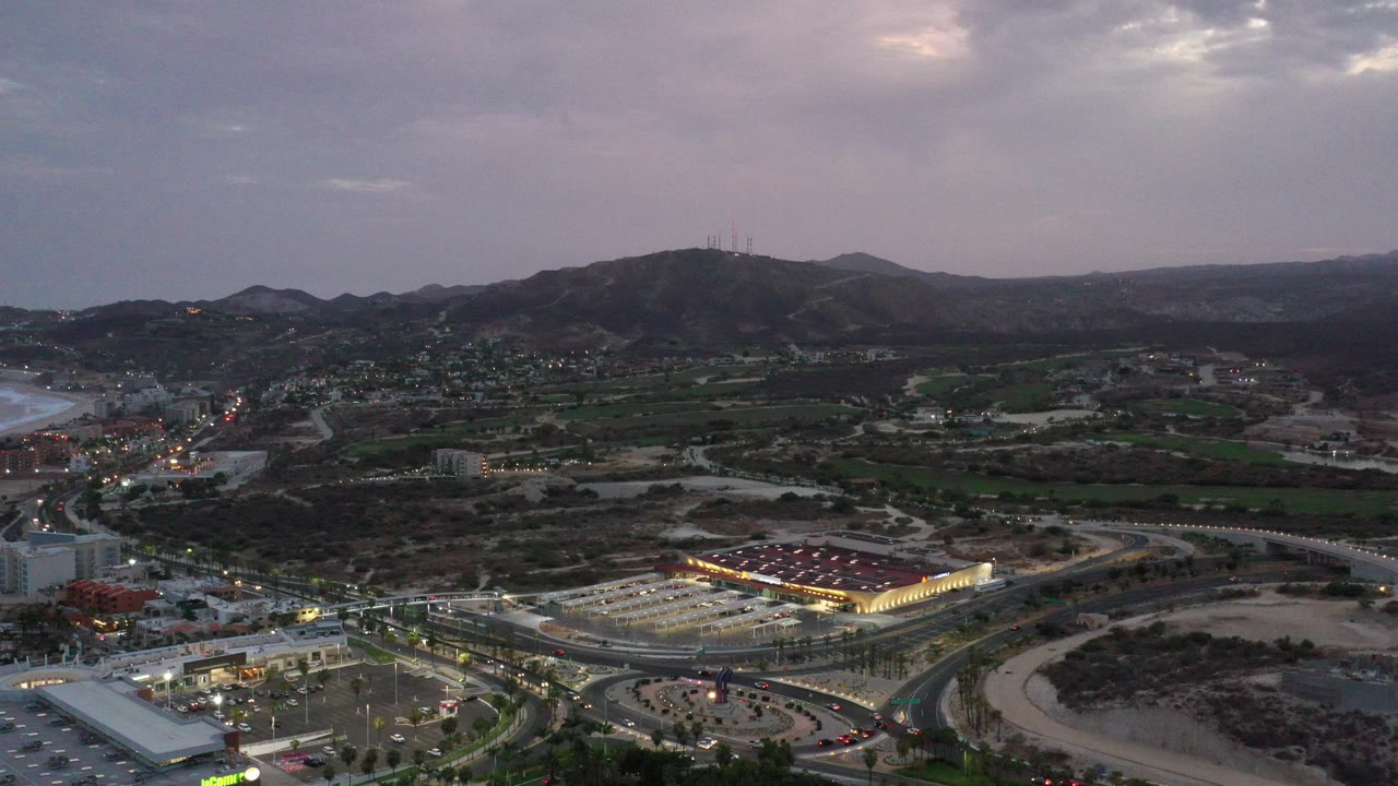 Wide aerial view of roads, buildings, hills, and cloudy sky at dusk.