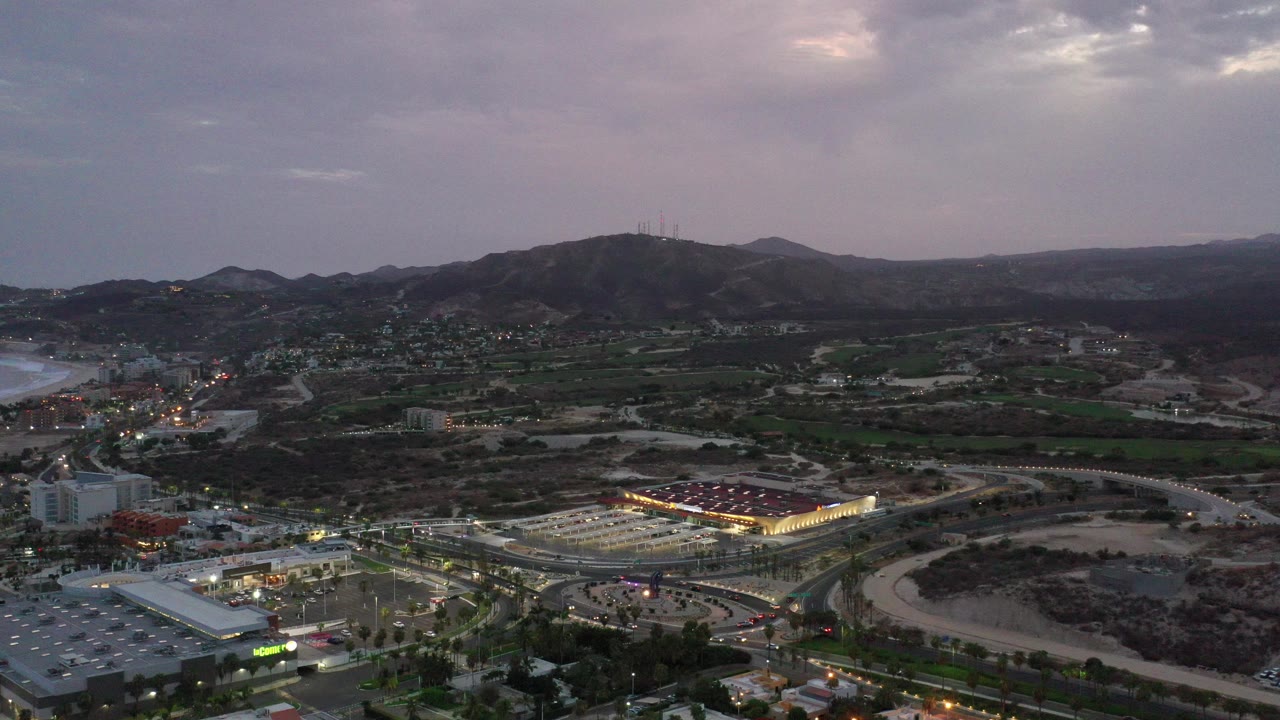 Wide aerial view of roads, buildings, hills, and a cloudy dusk sky.