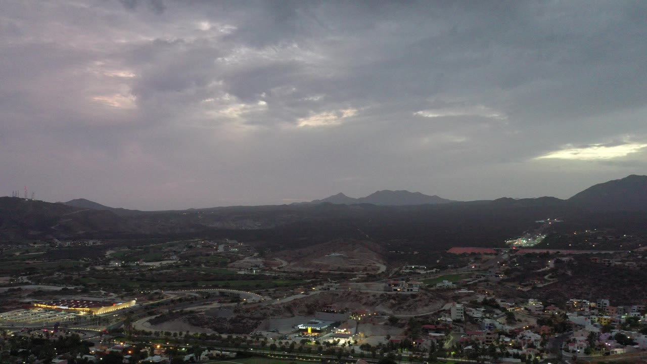 Elevated evening view over a town, hills, and cloudy sky.