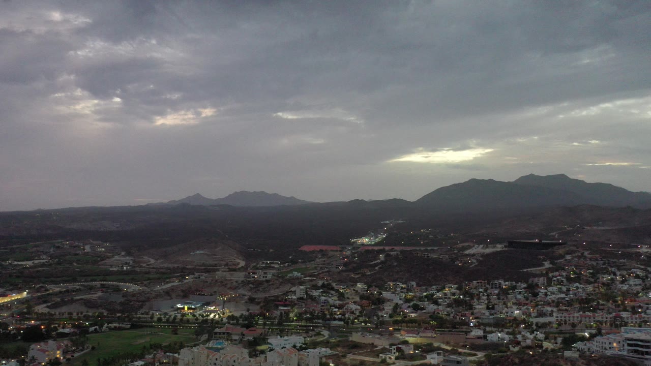 Los Cabos, Mexico appears from an elevated wide view with city buildings and road lights below dark mountain ridges, with no visible people.