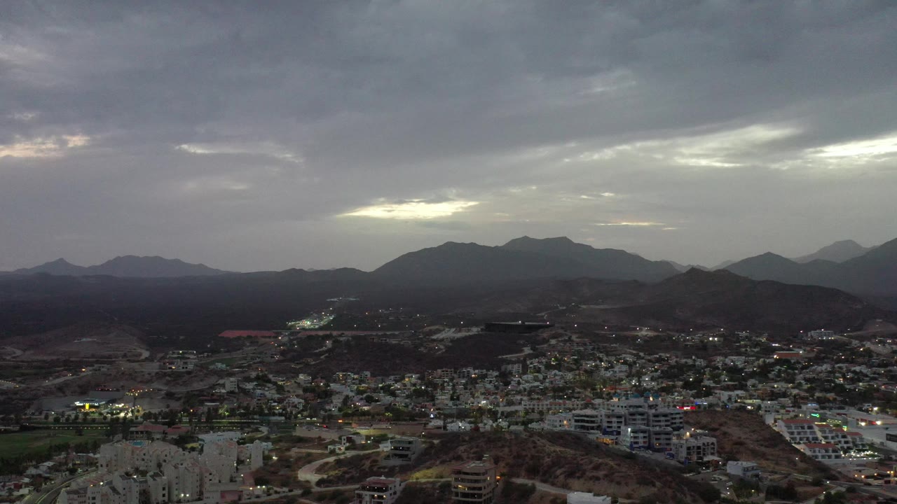 Urban area at dusk beneath heavy clouds and distant mountains.
