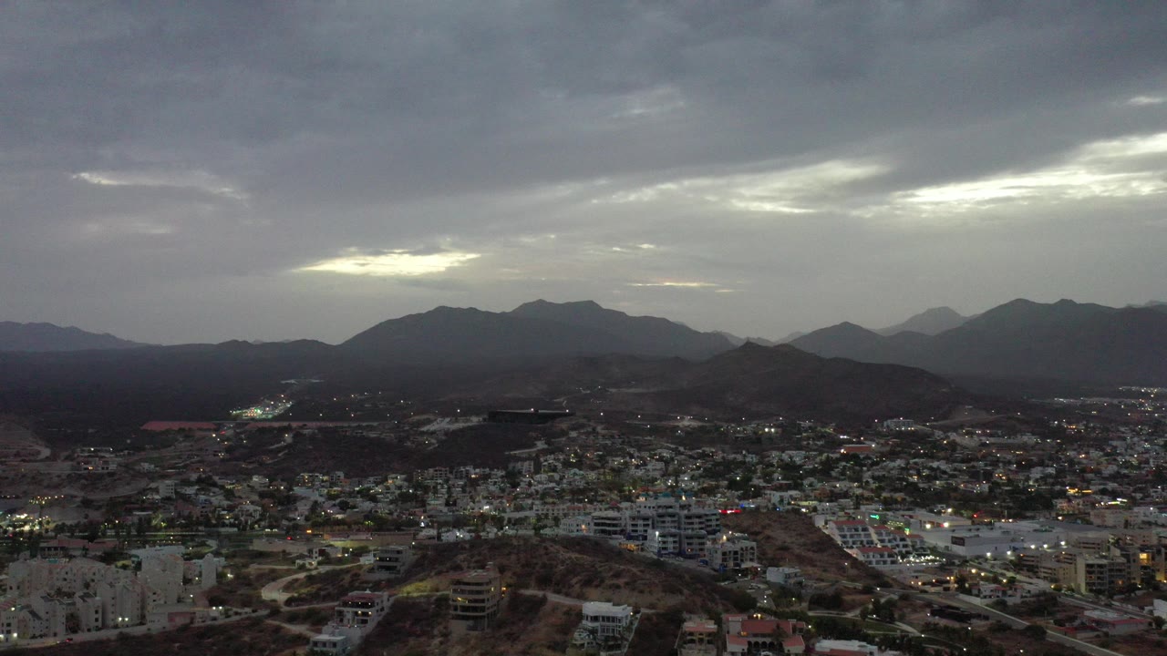 Wide aerial view of a city below dark mountains and rain clouds.