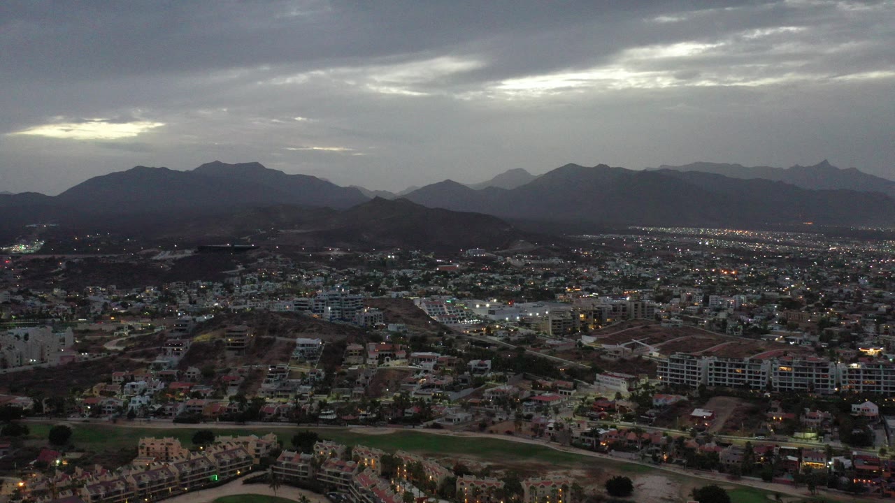 Aerial view of a city below dark mountains and a cloudy sky.