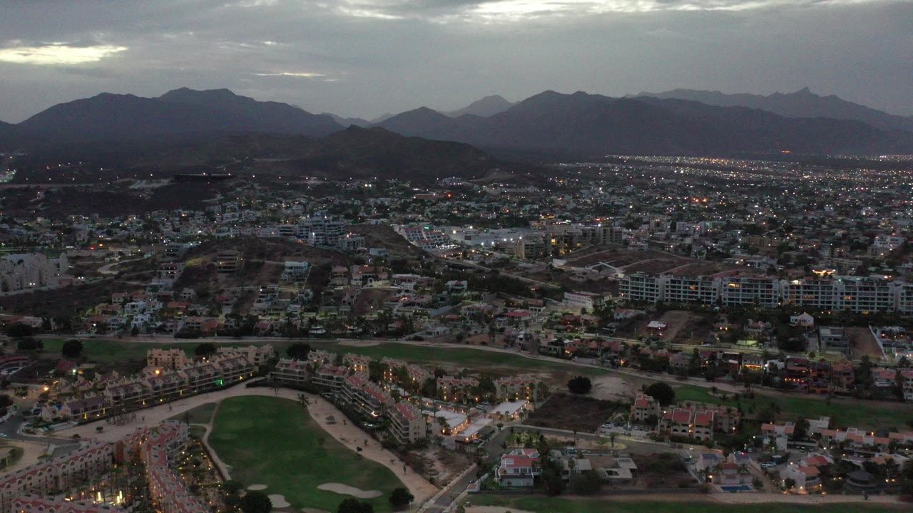 Wide aerial city view with mountains and a golf course at dusk