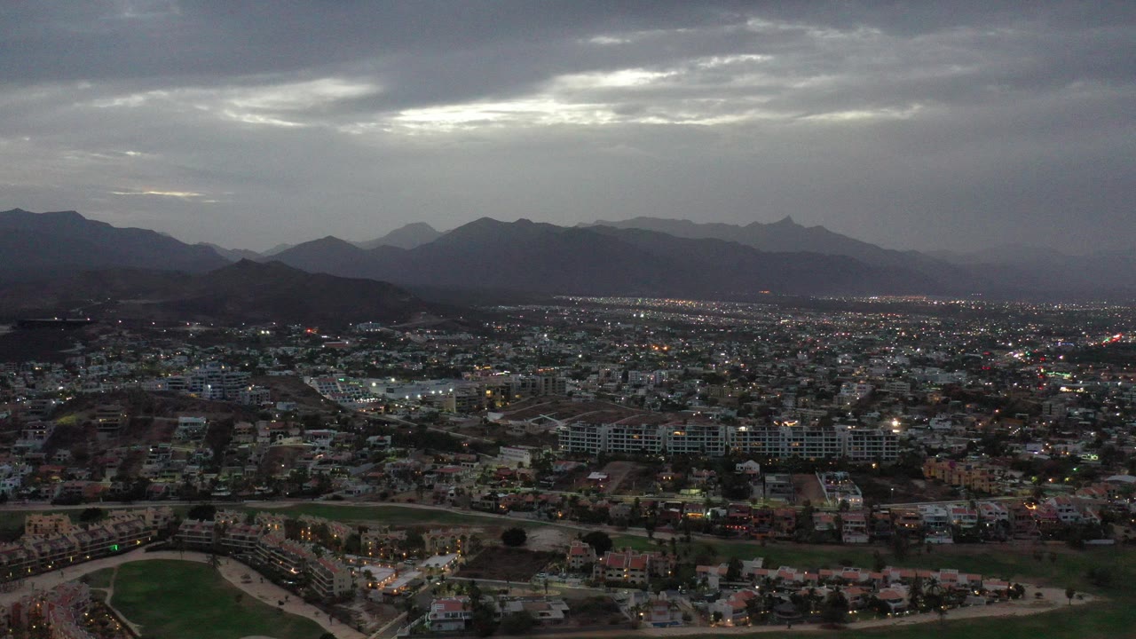 Wide aerial city view under dark clouds and mountain horizon