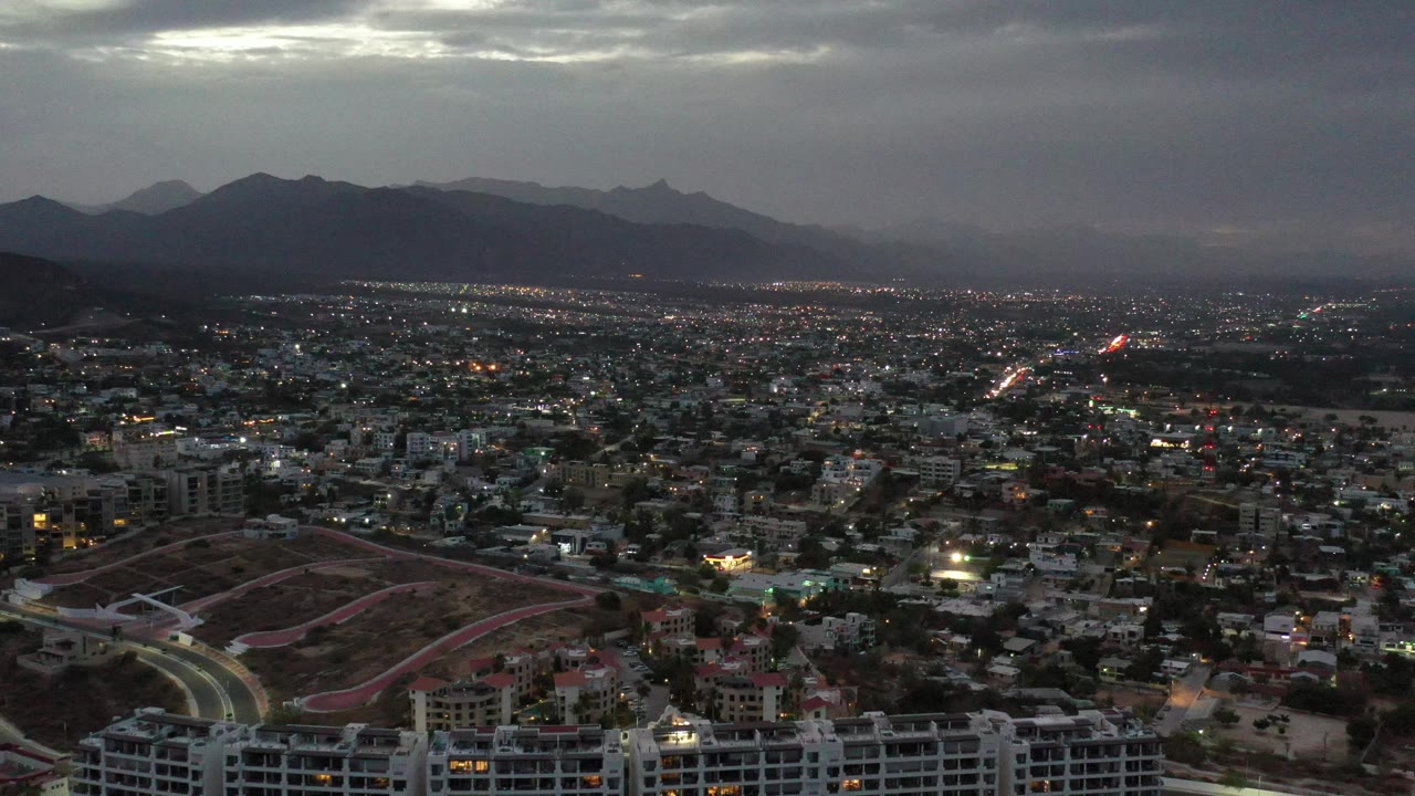 City skyline and mountain ridge under darkening clouds.