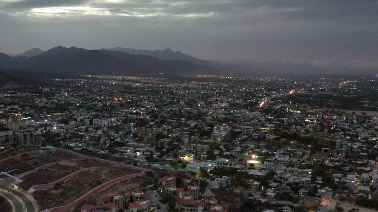 Aerial cityscape beneath gray clouds and distant mountains.