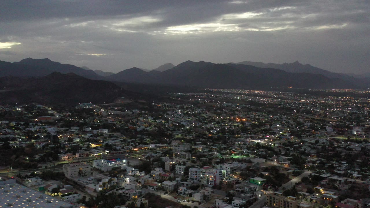 Dusk aerial view over a city with mountains and heavy clouds