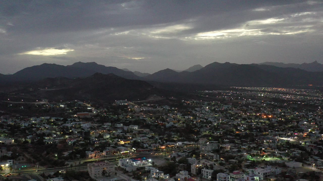 Aerial dusk view of a town below dark mountains and cloudy sky.