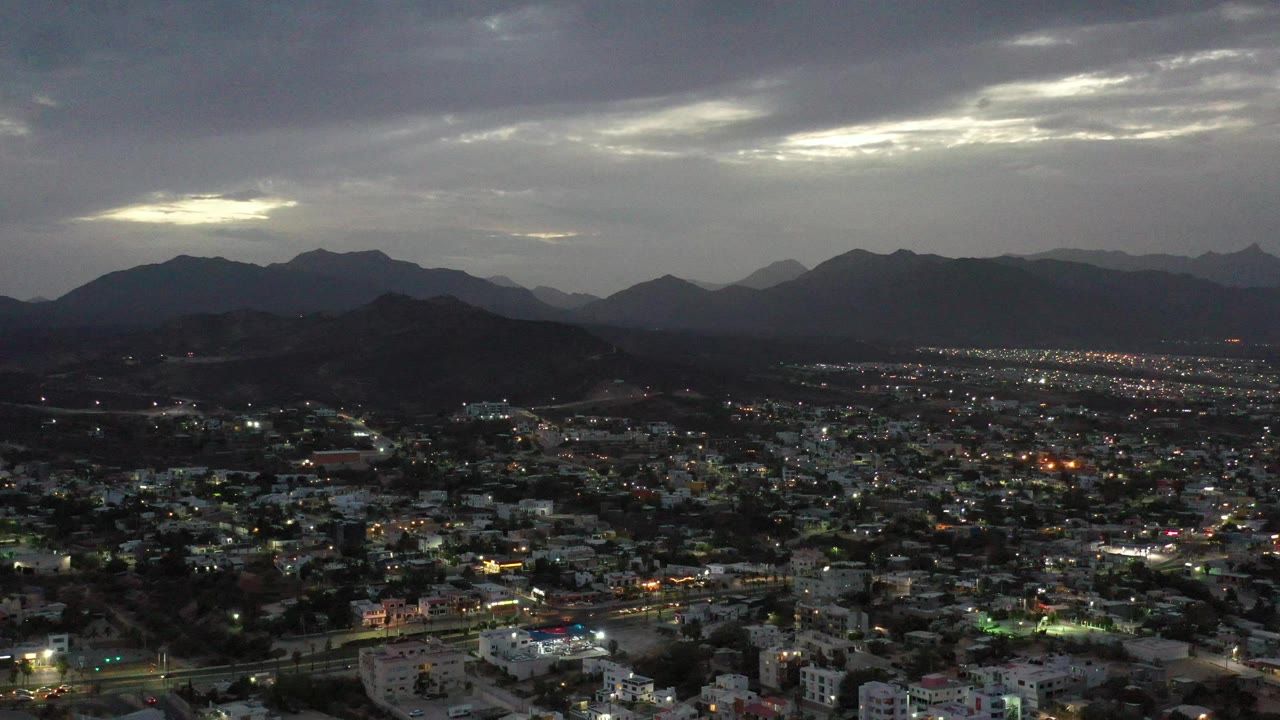 Dense nighttime neighborhood with road lights and distant mountains.