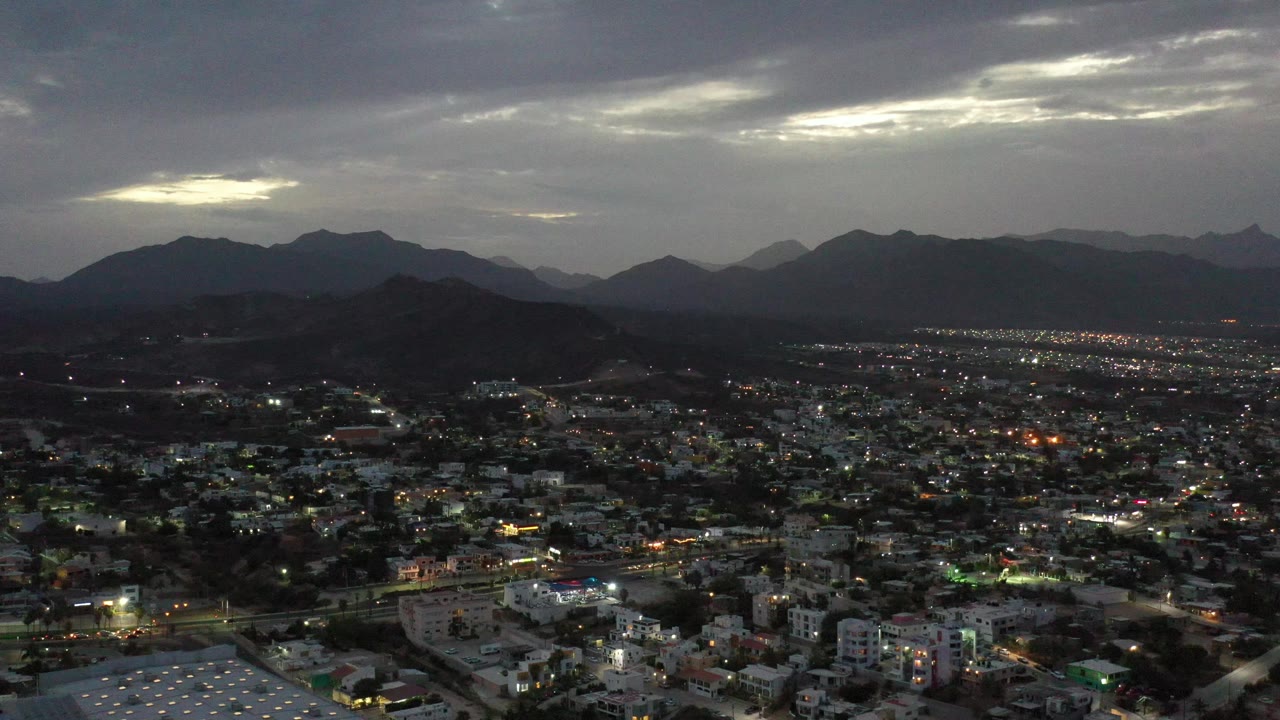 Cloud break above a lit city and distant mountain ridge.