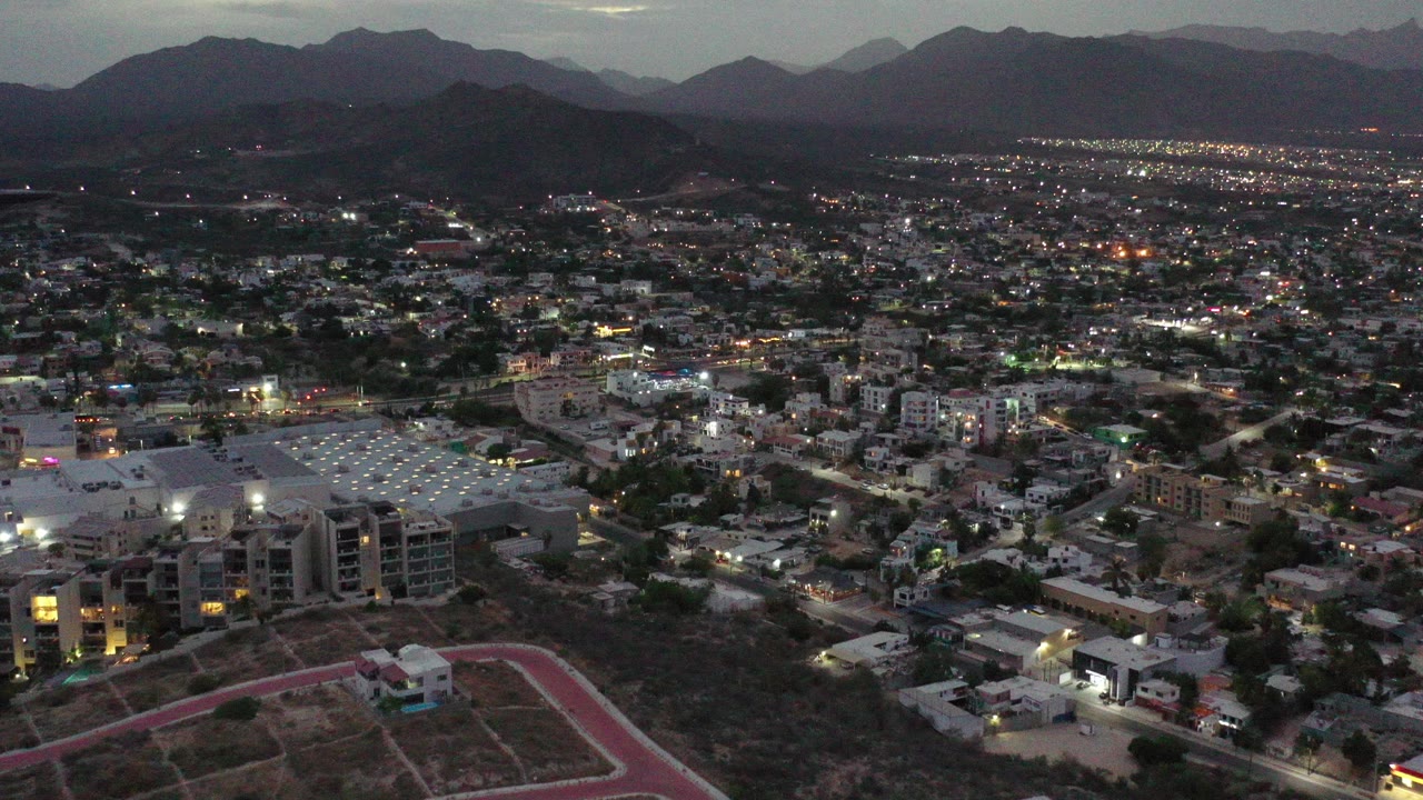 Aerial dusk view over a Los Cabos suburb with mountains beyond.