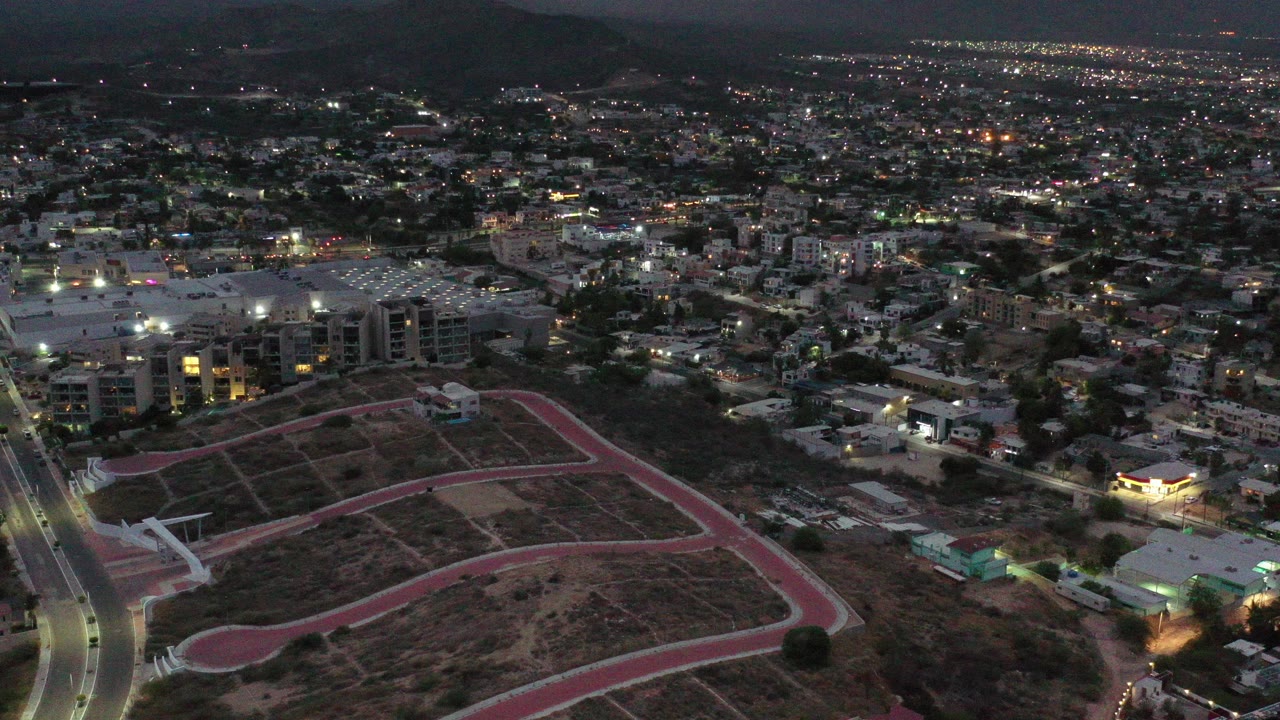 Night aerial view of city lights, roads, buildings, and dark mountains.