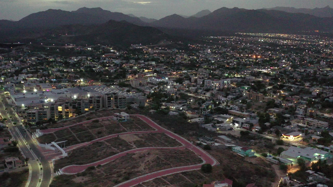 Aerial dusk view over a lit city with mountains in the distance.
