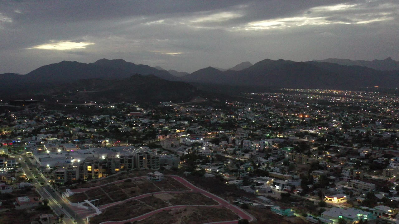 Dusk aerial over a city with mountains under cloudy sky