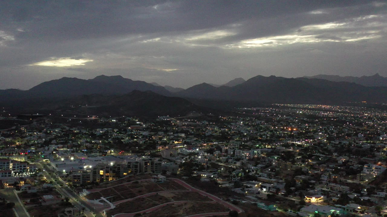 Aerial view of a town below dark mountains and a cloudy sky.