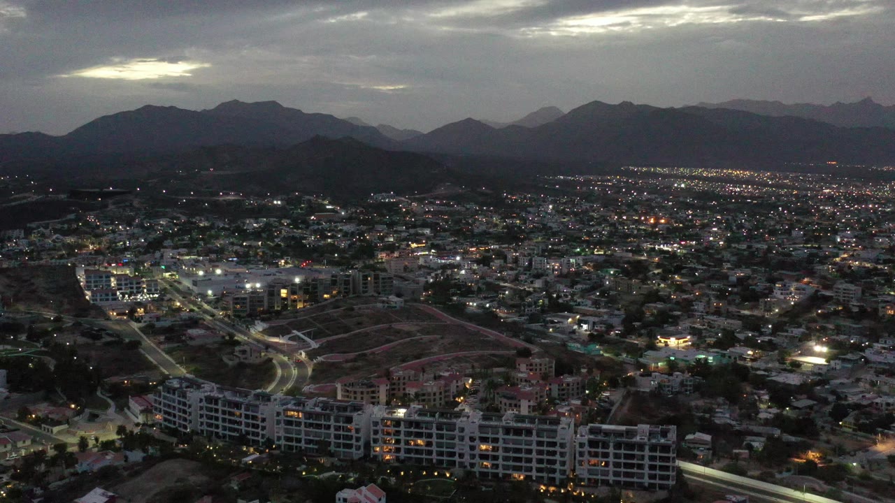 Dusk aerial over city lights with foreground apartments and distant hills