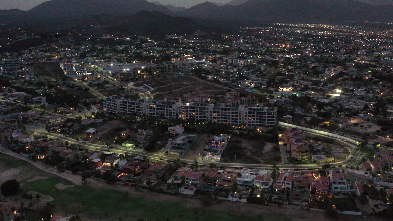 Aerial night view over a lit residential neighborhood with mountains in the distance