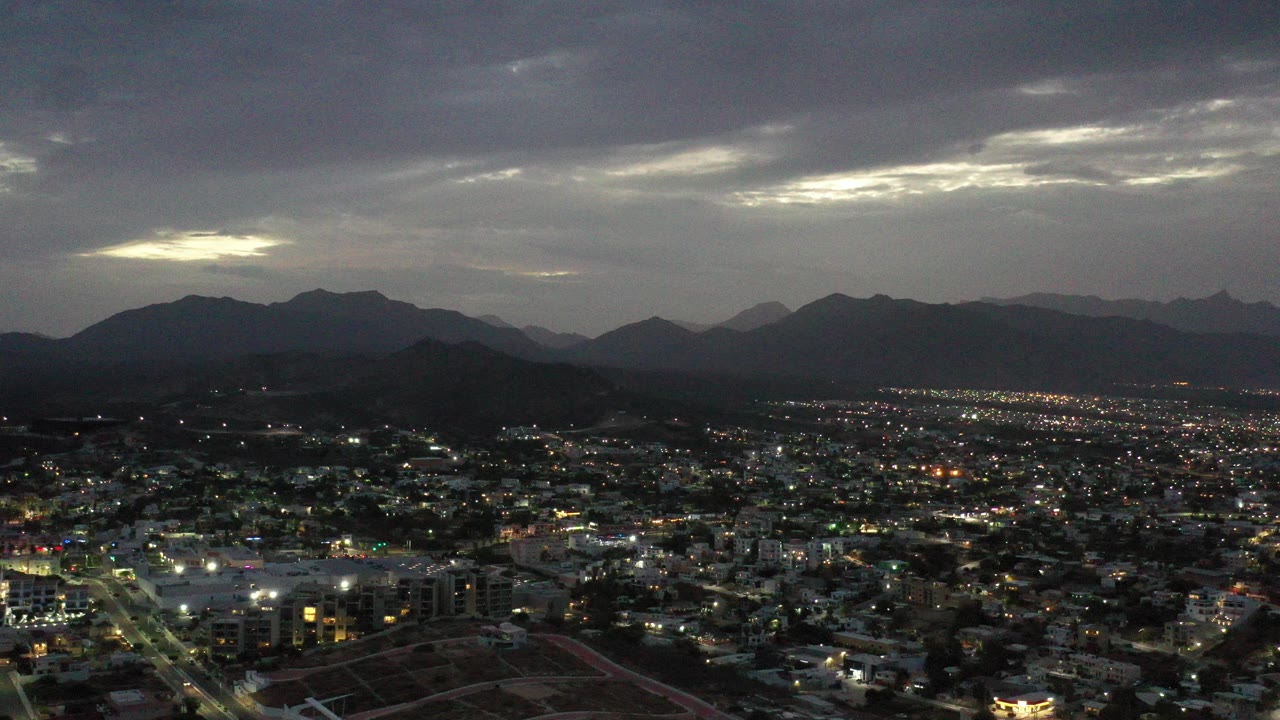 Cloudy dusk aerial over city lights and mountain silhouettes