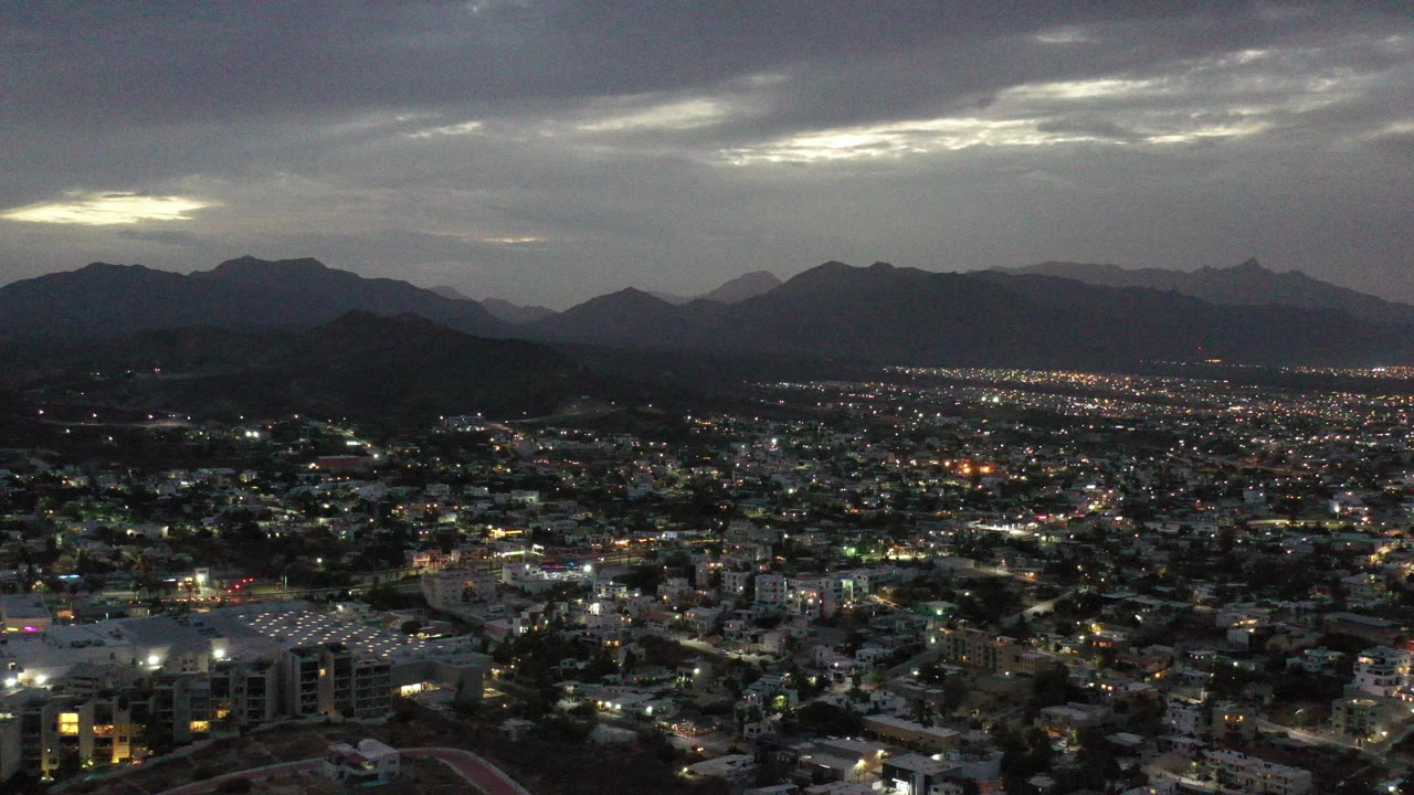 Aerial city lights below dark mountains and gray clouds