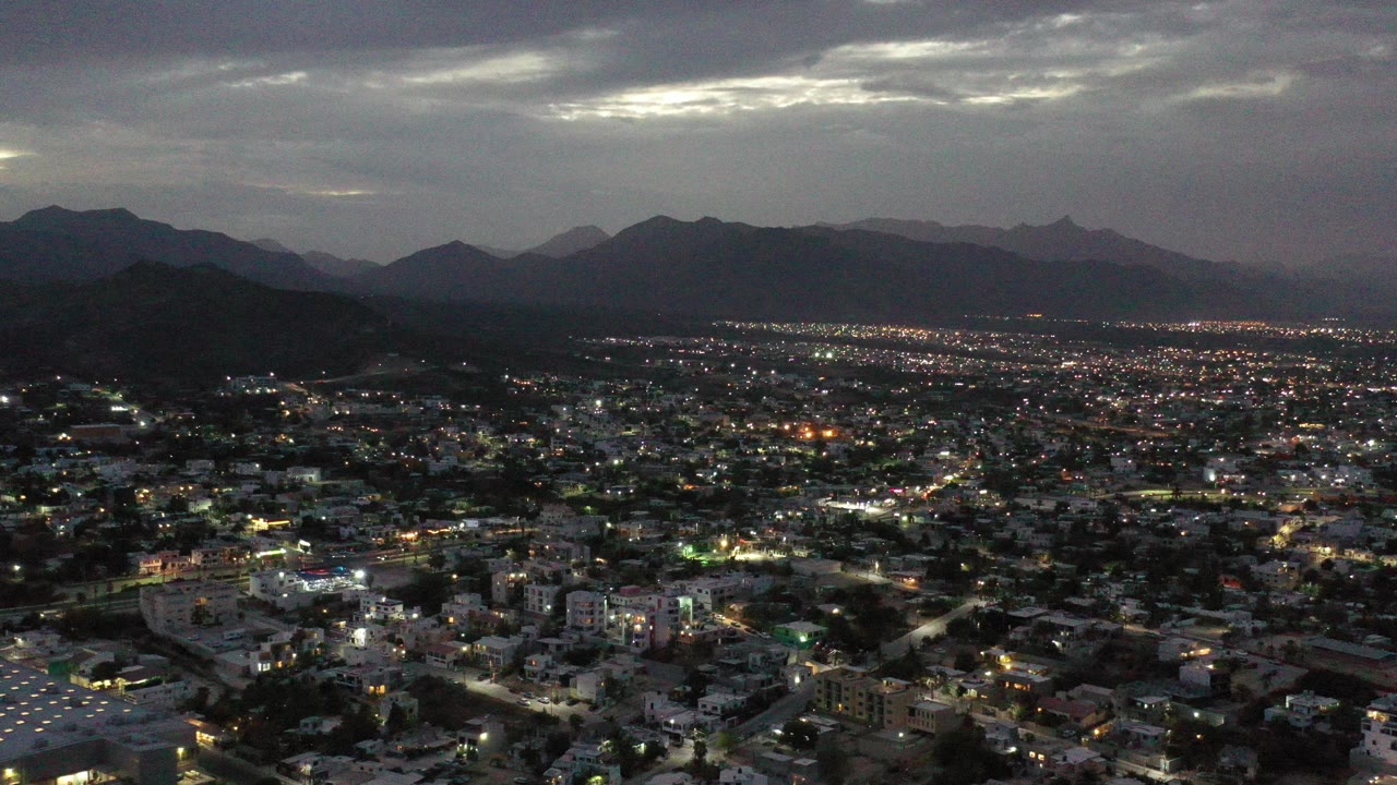 Aerial view of city lights below dark mountains at dusk.