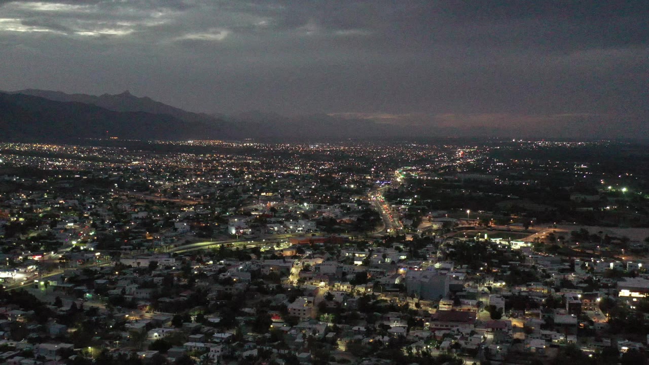 Aerial night cityscape with dense lights and a dark mountain range on the horizon.