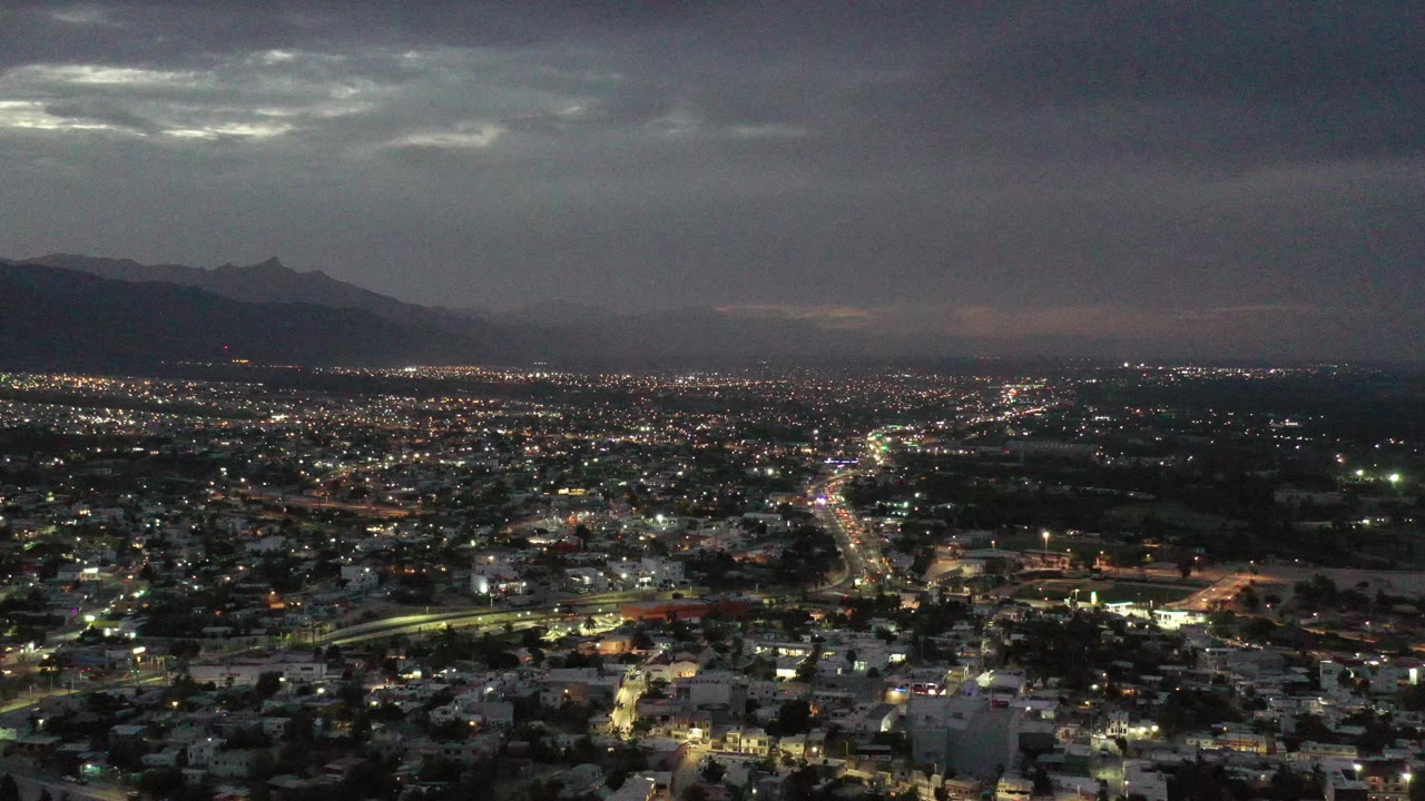 Evening city lights with mountains and low clouds.
