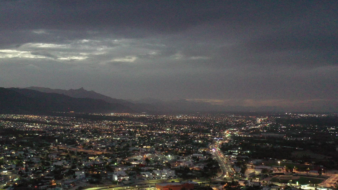 Wide city lights beneath a gray sunset sky and distant mountains.
