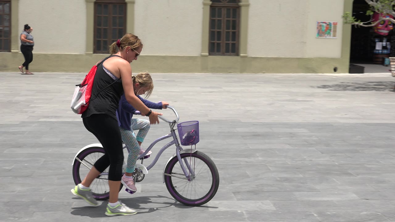 The woman stays close behind the young rider in Los Cabos, Mexico, holding near the bicycle as the child keeps both hands on the handlebars.