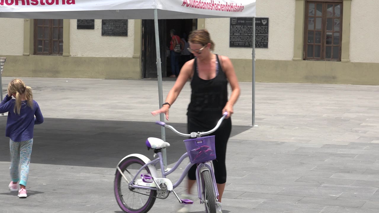 Woman pushing a purple bicycle as a young girl walks across a plaza.