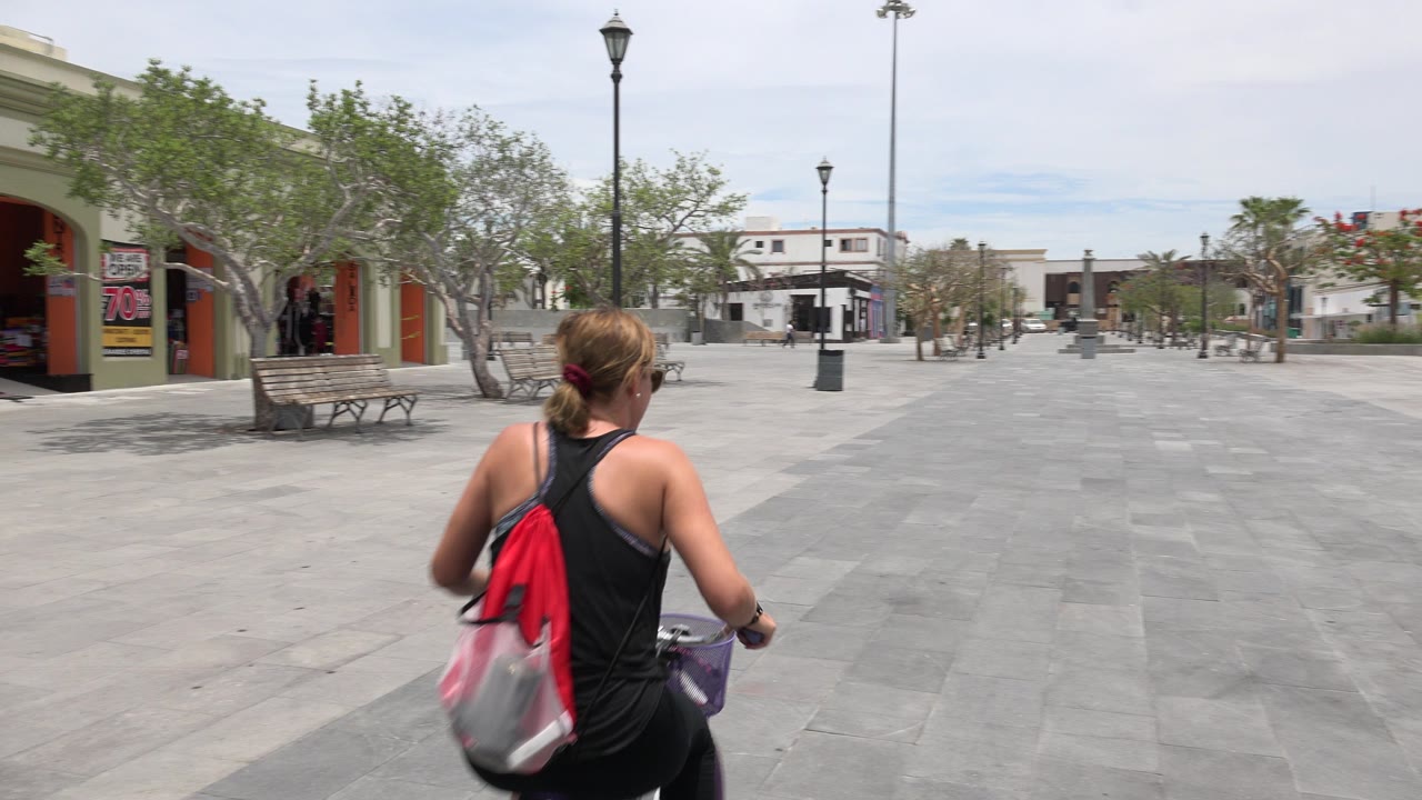 Woman cyclist entering a wide paved plaza from the foreground.