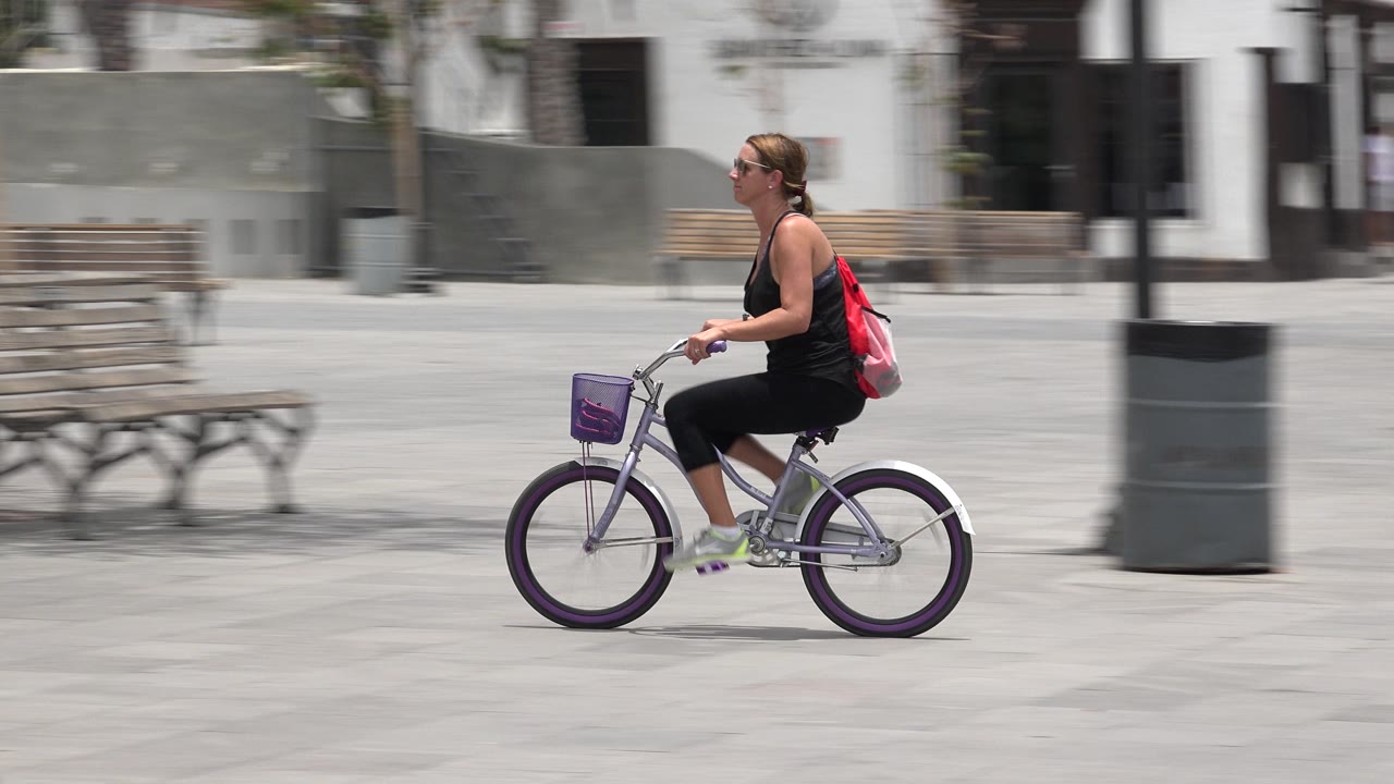 Woman riding a small bicycle across a paved plaza.