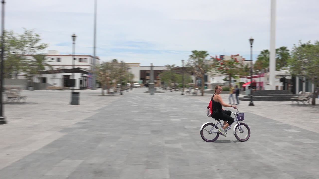 Adult riding a purple bike across a paved plaza.