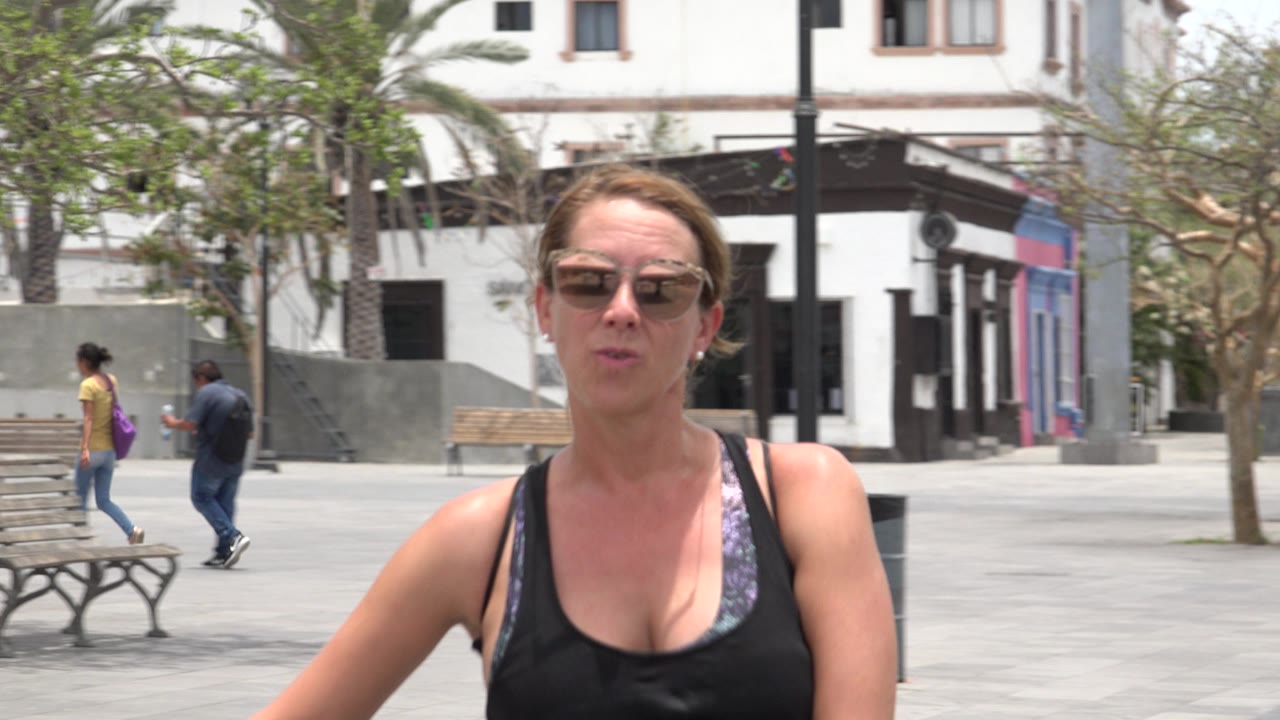 Woman in sunglasses facing camera in a sunny plaza.