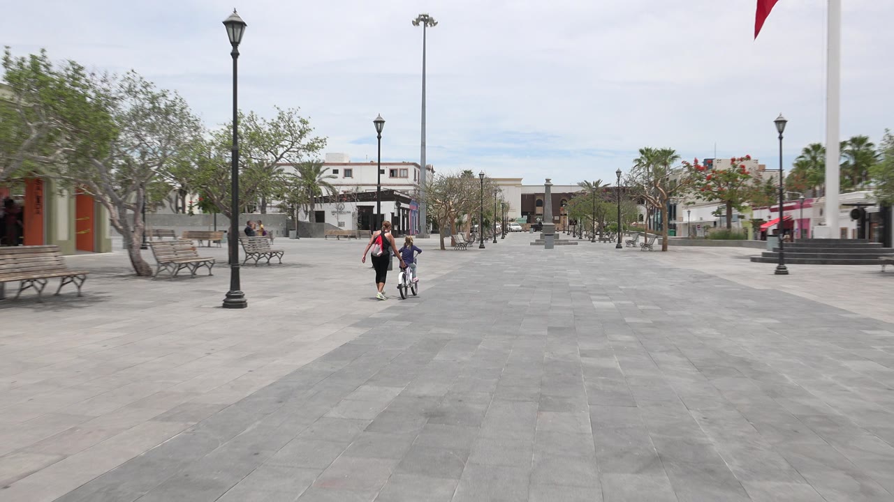 Mother and child with bicycle in a wide plaza.