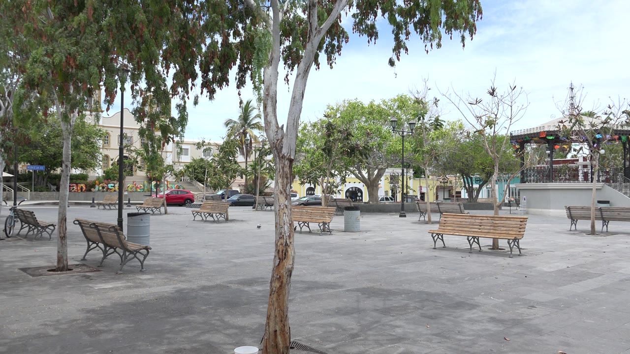 Wide paved town square with benches, trees, and parked cars.