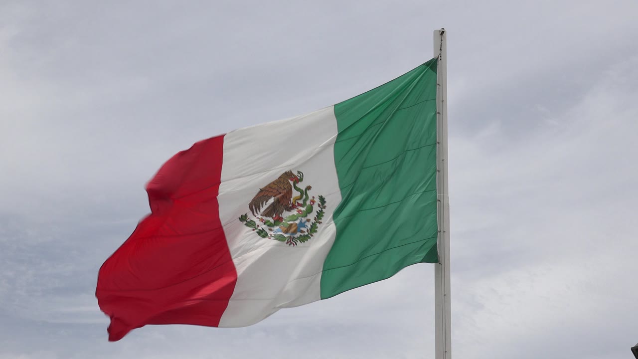 Mexican flag in Los Cabos, Mexico billows outward with the red section curling and the green section held near the pole, no visible people.