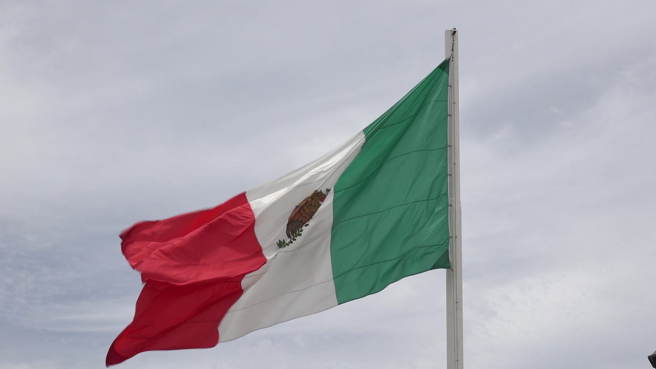 Mexican flag pulled taut and folded in strong wind.