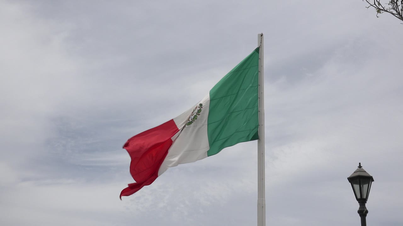 The Mexican flag remains high on the pole in Los Cabos, Mexico, its red and white sections pulled outward while the green panel sits nearest the pole, with no visible people.