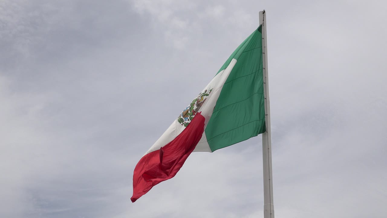 Mexican flag on a pole against gray clouds.