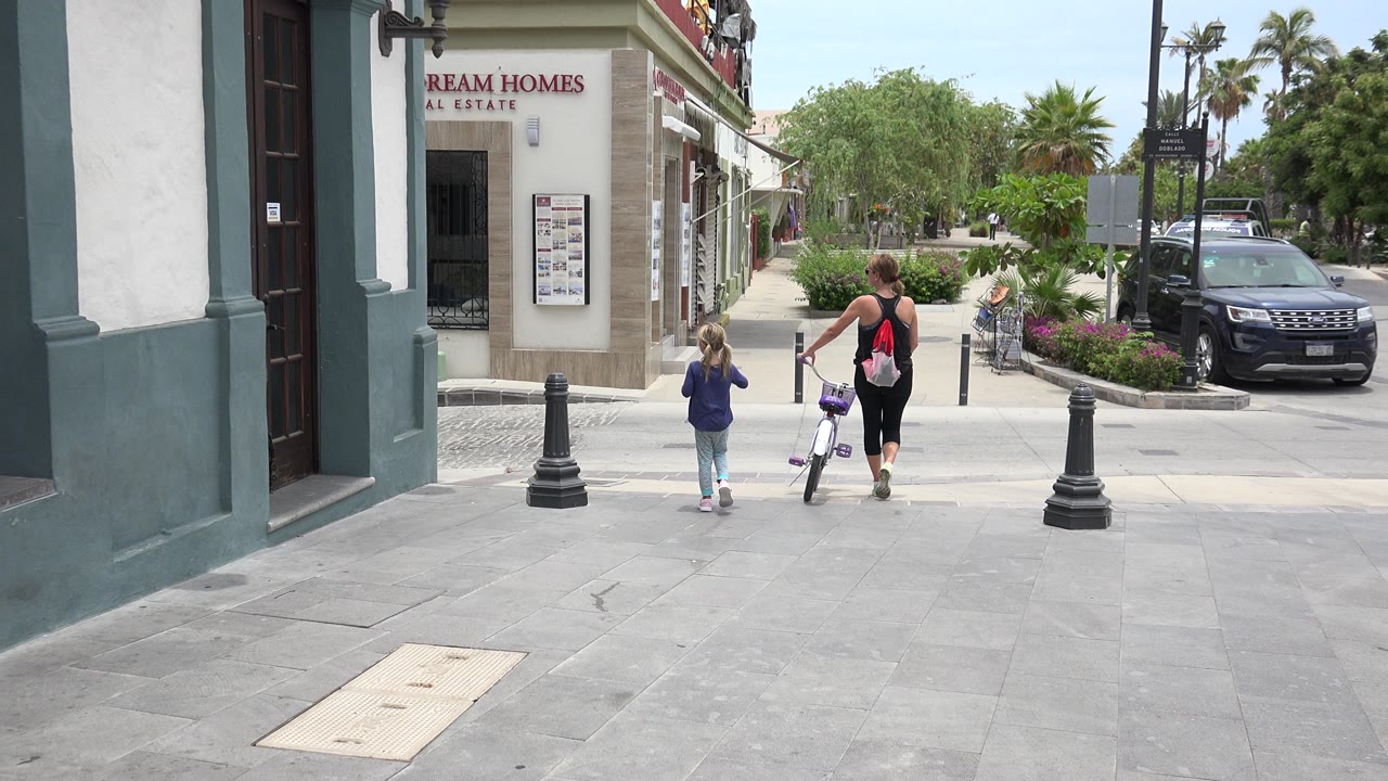 Woman and child walking away on a sidewalk beside a small bicycle.