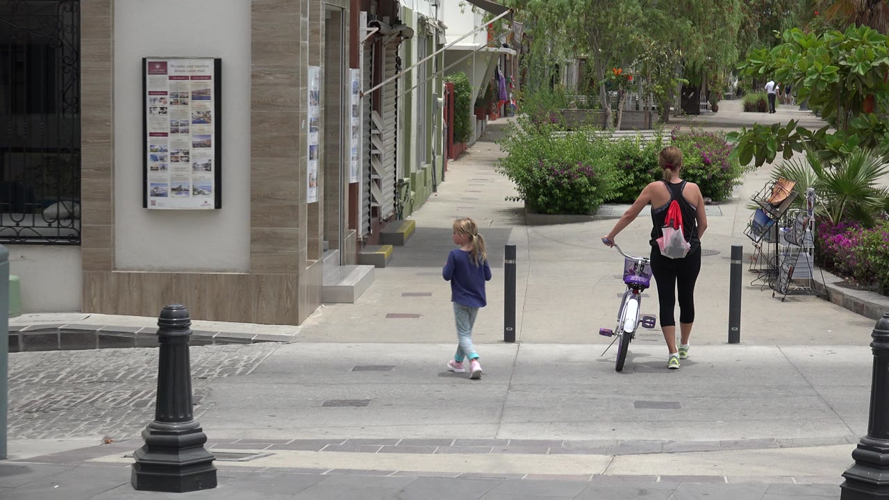 Adult with bicycle and child entering a landscaped walkway from a street curb.