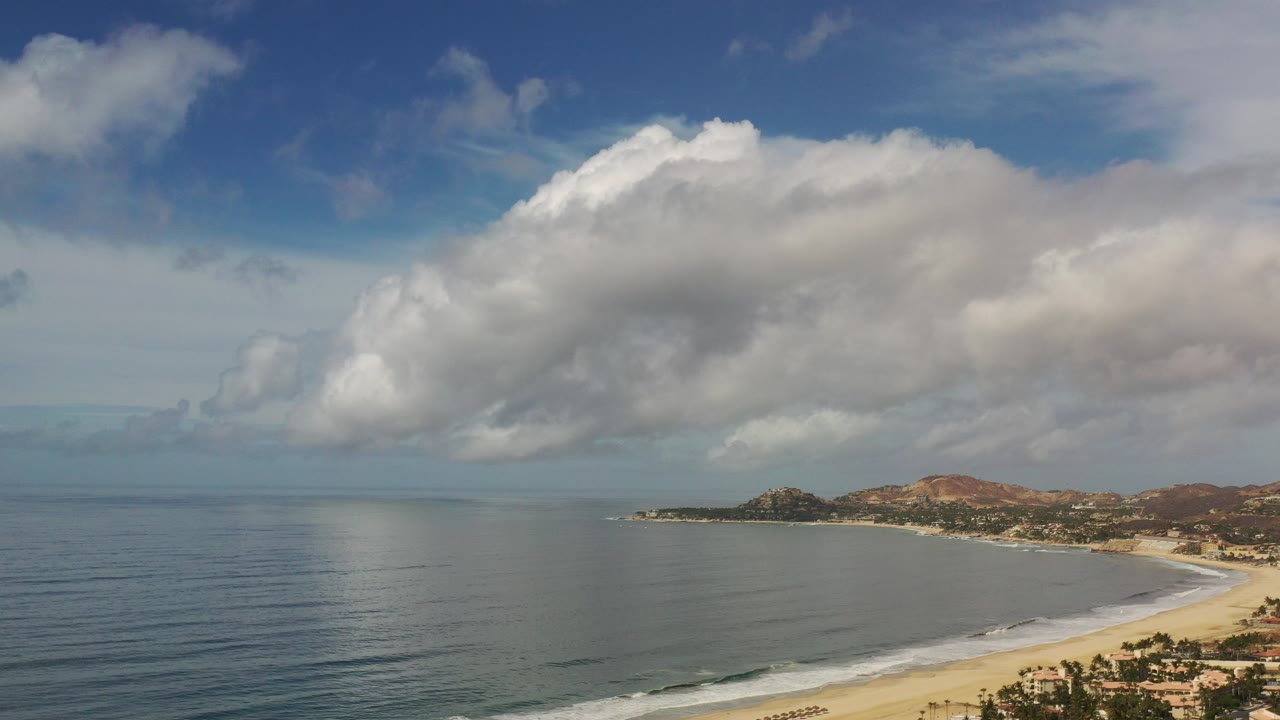 Wide aerial view of ocean, beach, mountains, and large clouds.