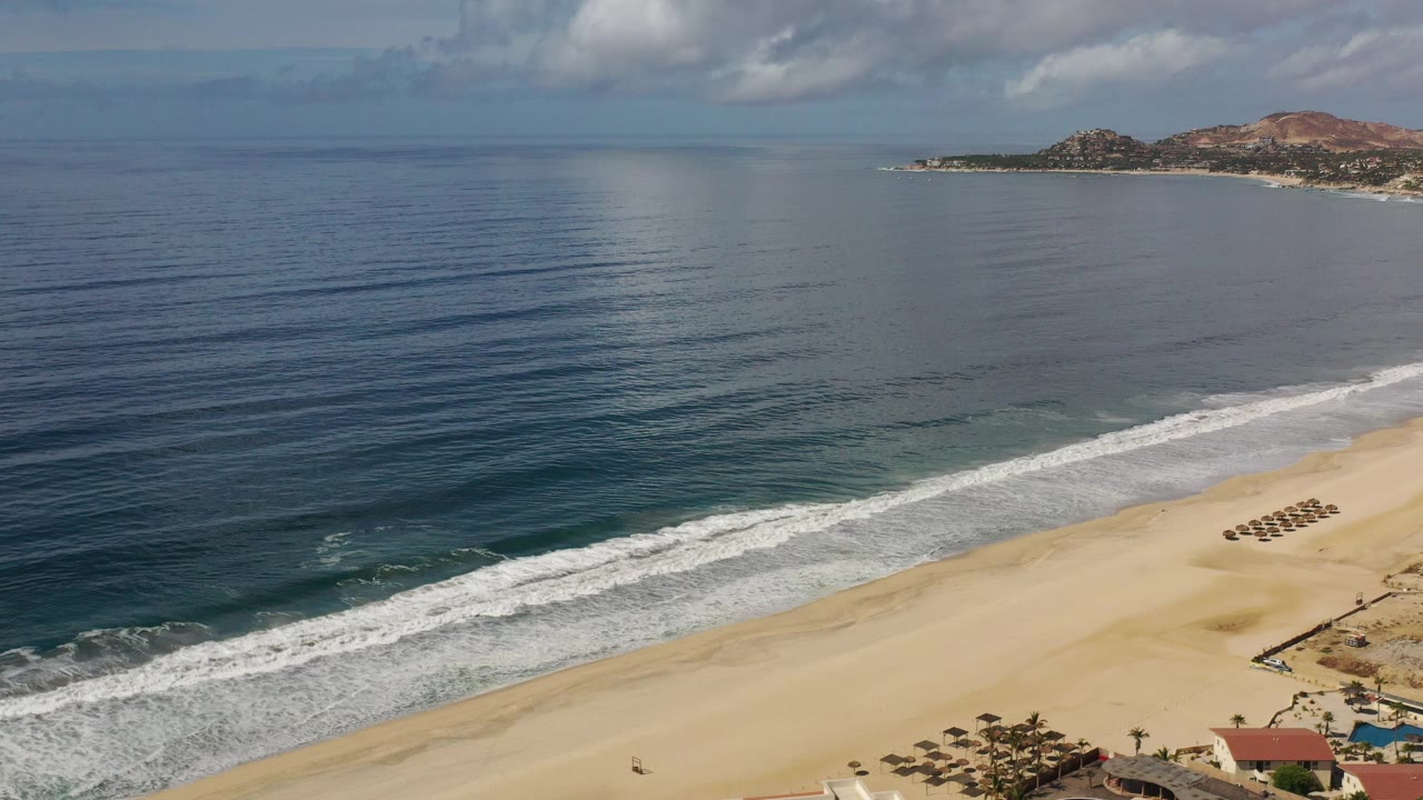 Aerial view of ocean surf meeting a wide sandy beach with beachfront buildings below.