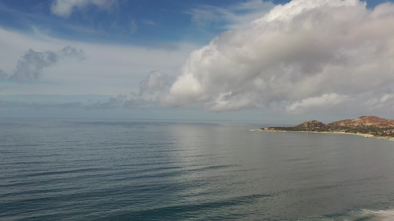 Wide ocean view with large clouds and a distant coastline at right.