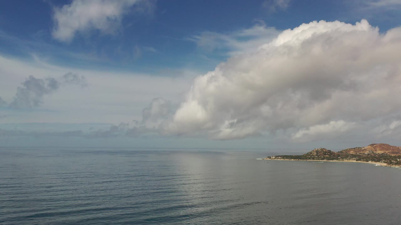 Wide Los Cabos water view with a large white cloud over the sea, low coastline on the right, and no visible people.