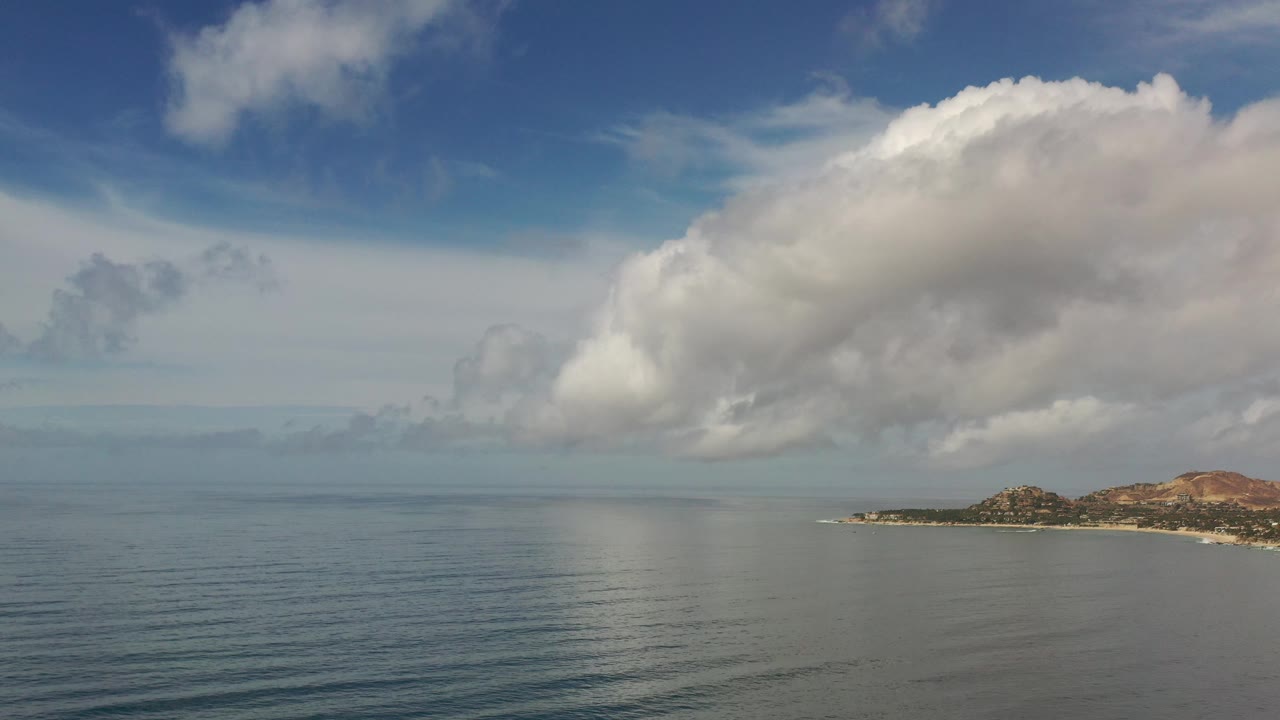 Open sea below a bright cloud with distant coast at right
