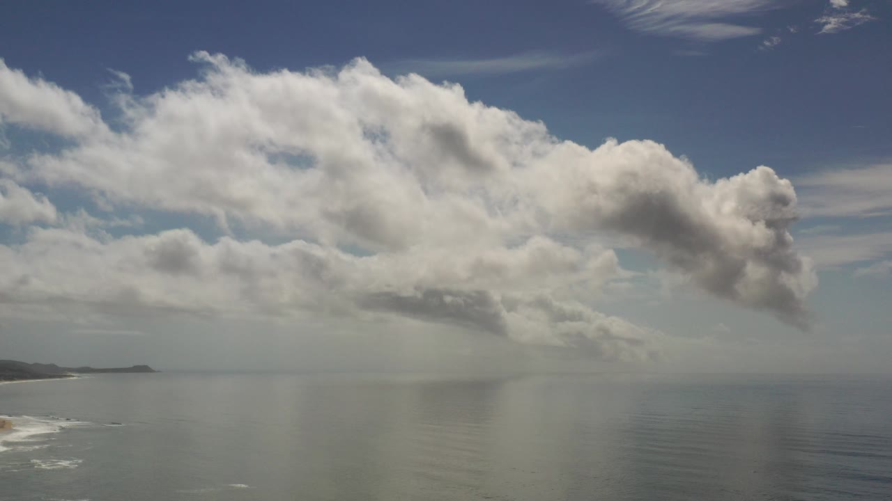 Cloud bank over ocean horizon with coastline at left.
